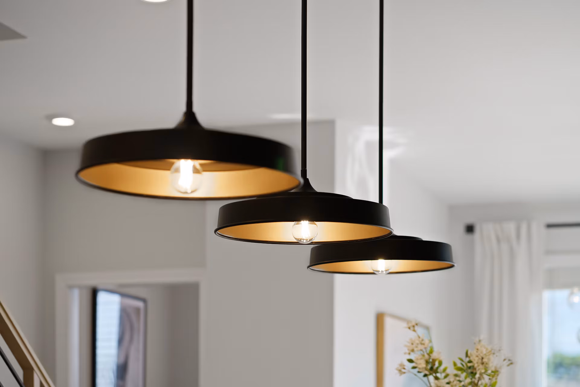 Three black pendant lamps with golden interiors hang from the ceiling in a bright, minimalist room.